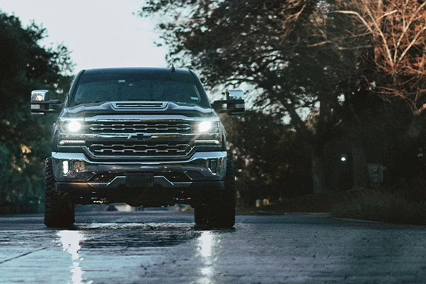 Chevrolet diesel truck facing forward with headlights on parked on rainy parking lot